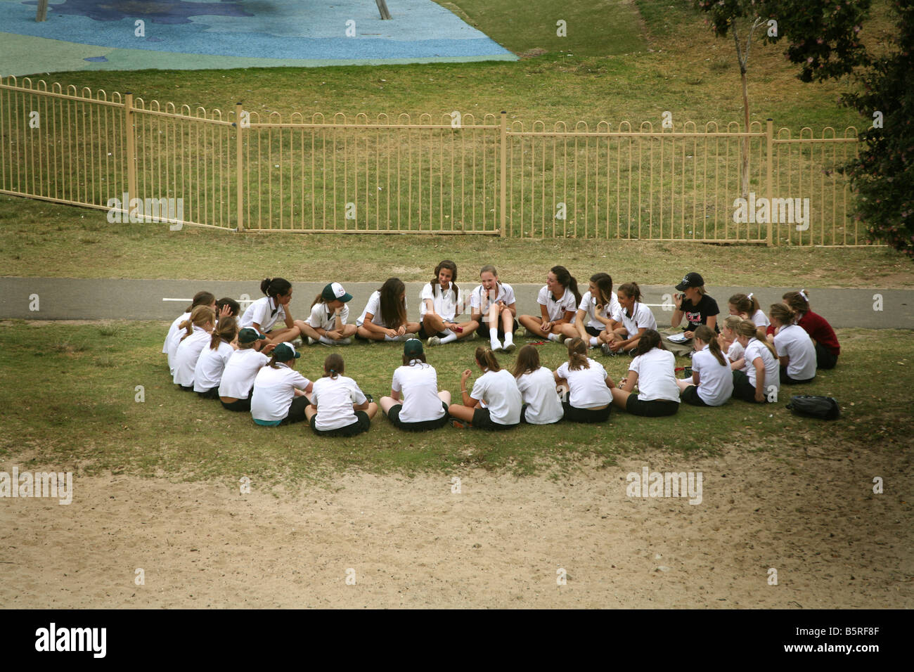 Una classe di studentesse di sedersi con il loro insegnante all'aperto, in una ambiente di istruzione Foto Stock