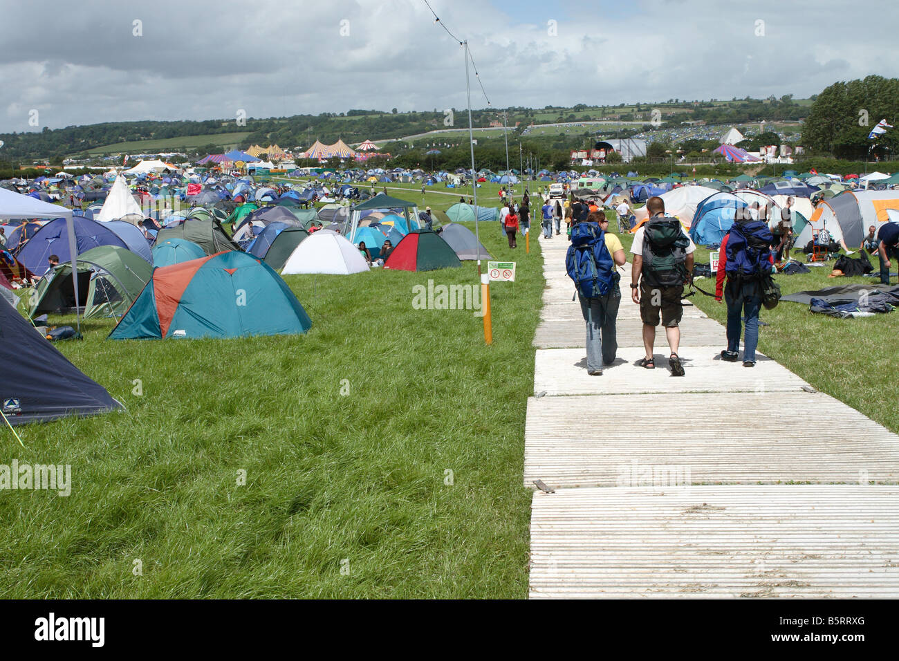 Glastonbury Festival pop fans camminando sulla pavimentazione in metallo attraverso la tenda area camping il primo giorno f il festival nel mese di giugno 2008 Foto Stock