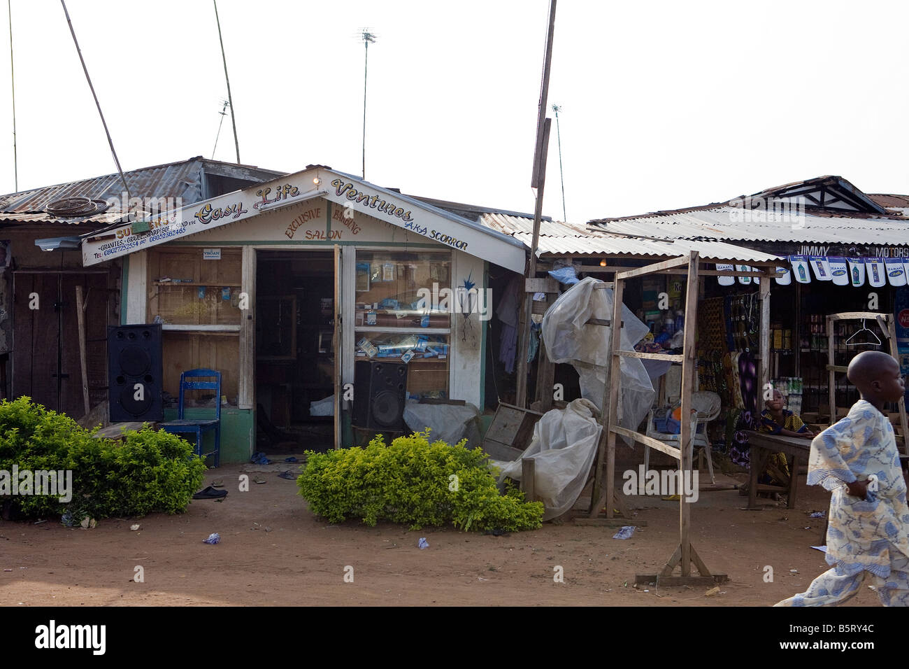 Un giovane ragazzo ha appena eseguito passato un negozio sgangherato nel piccolo villaggio di Poka, Stato di Lagos, Africa Foto Stock