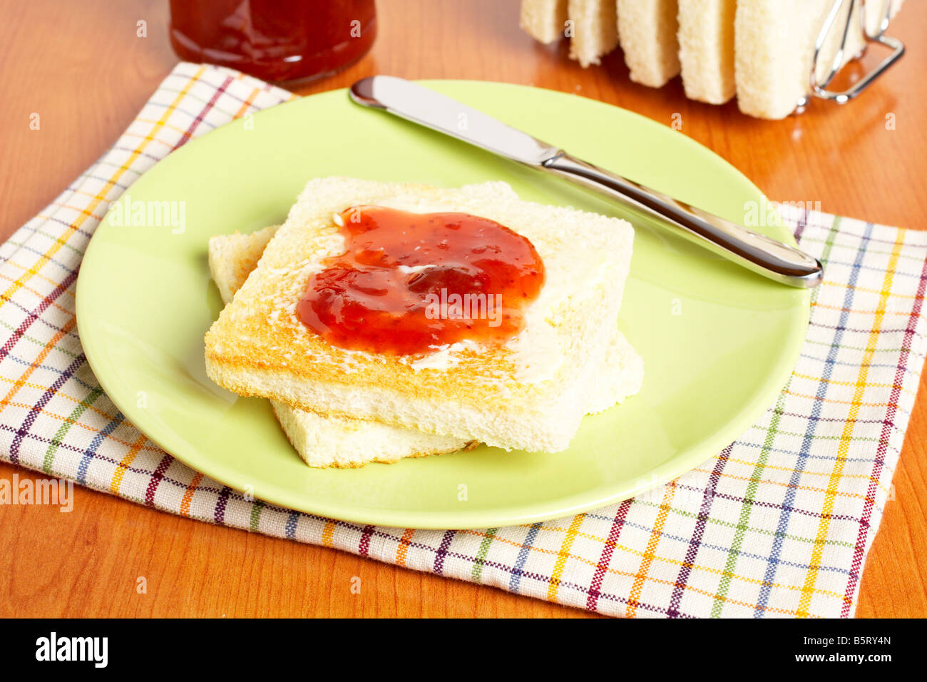 Toast con burro e marmellata di fragola il vasetto di vetro nella piastra bianca con morbida ombra su piazza sullo sfondo del tappeto di profondità del fie Foto Stock