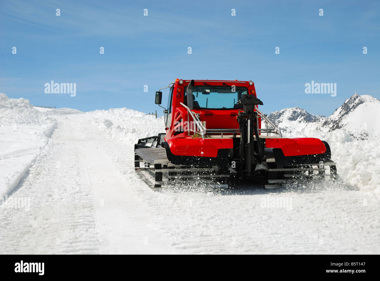 Rosso trattore catterpillar rende la strada di accesso sul pendio di neve contro il cielo blu, Pirenei Foto Stock