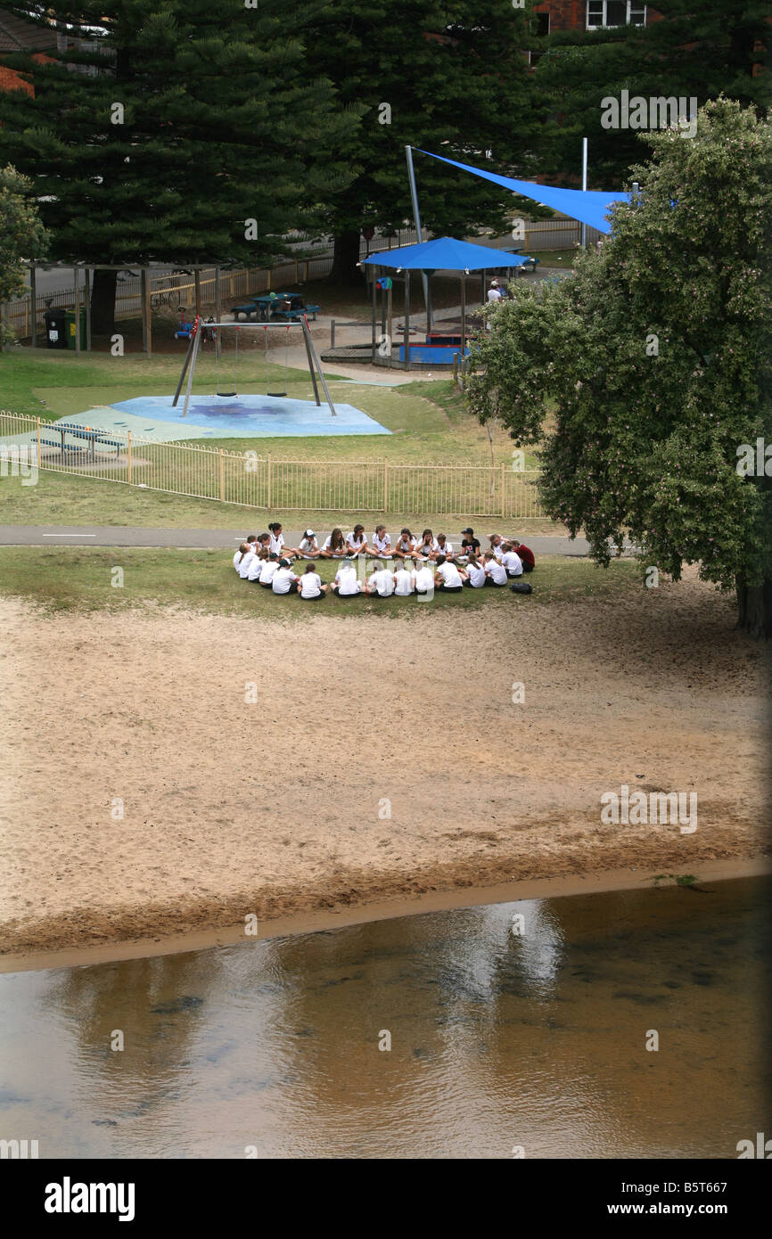 Una classe di studentesse di sedersi con il loro insegnante all'aperto, in una ambiente di istruzione Foto Stock