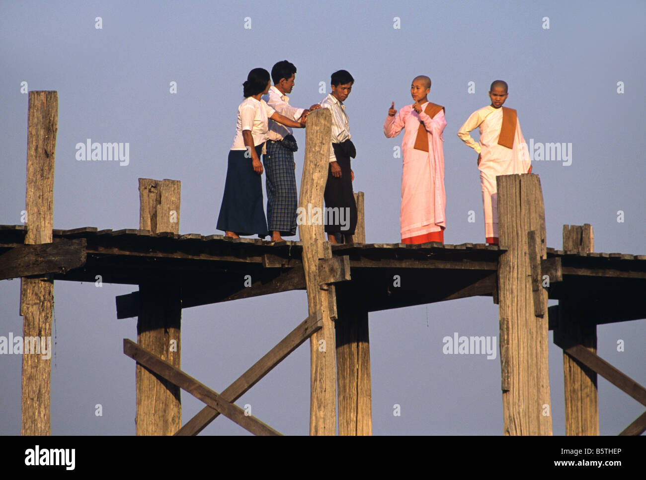 Birmane e monache buddiste cross U Bein's Bridge, la più lunga del mondo ponte in teak a lago Taungthaman, Amarapura, Mandalay Birmania Foto Stock
