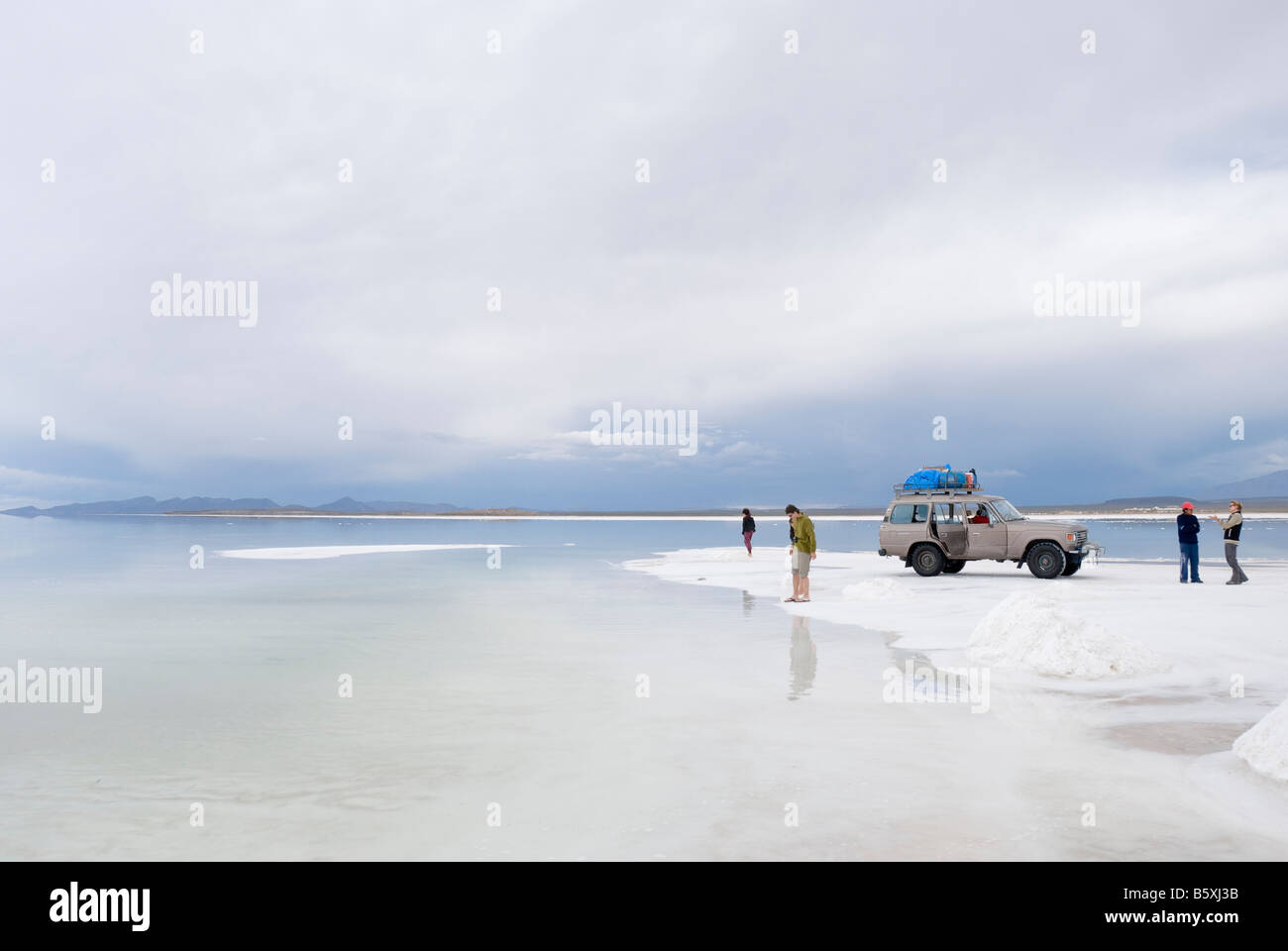 Un gruppo di turisti sostare vicino allagato acque del boliviano pianure di sale Salar de Uyuni Foto Stock