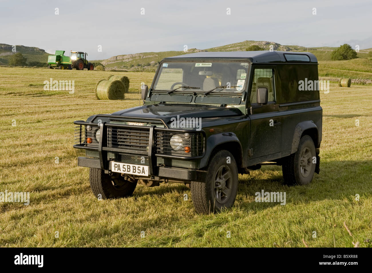 Un Landrover è in piedi in un campo, in background,l'agricoltore si imballa fieno. Foto Stock