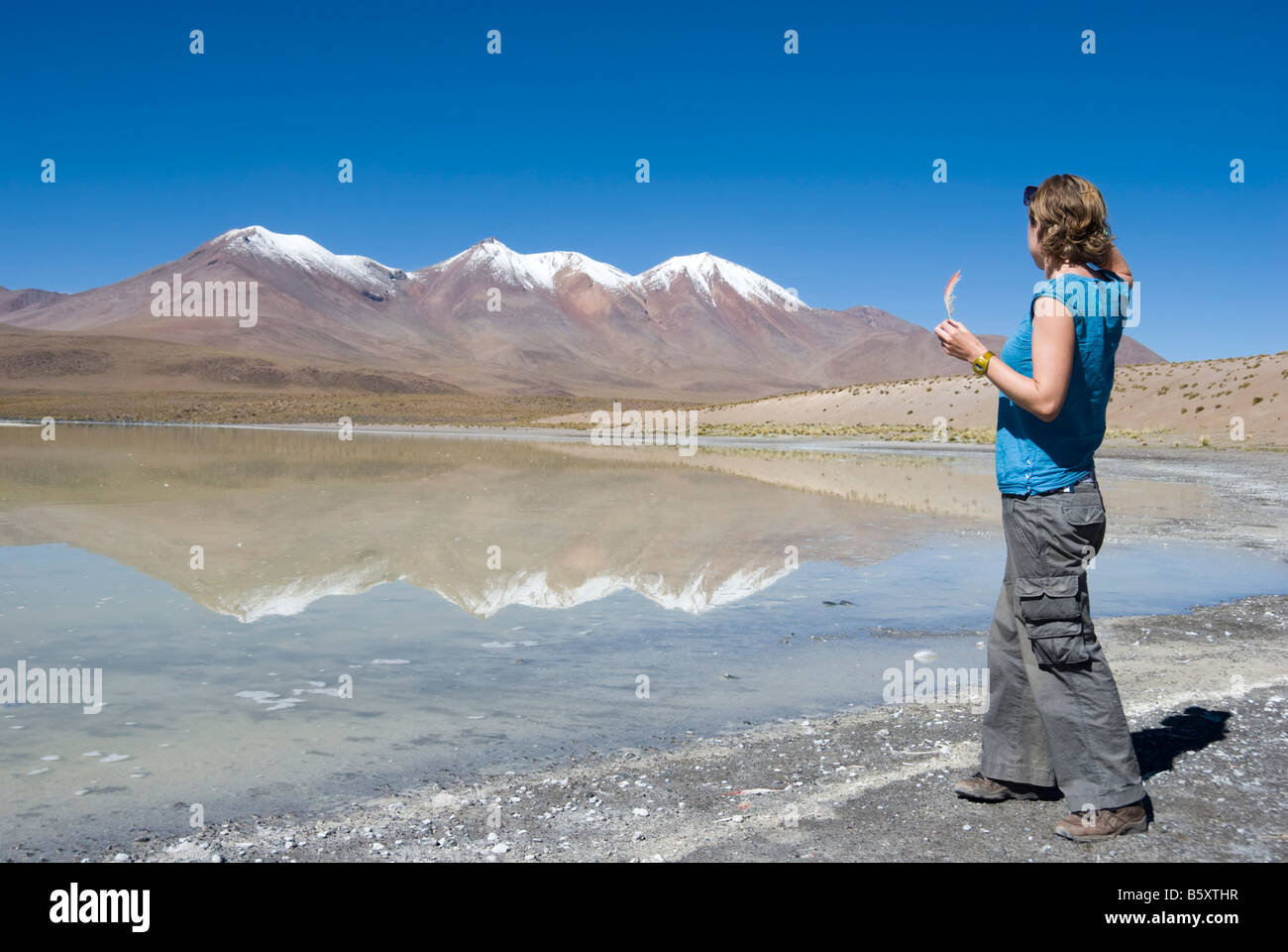 Un turista femminile (tenendo un flamingo giù) sorge accanto a Laguna Colorado nell'Altipiano boliviano. Foto Stock