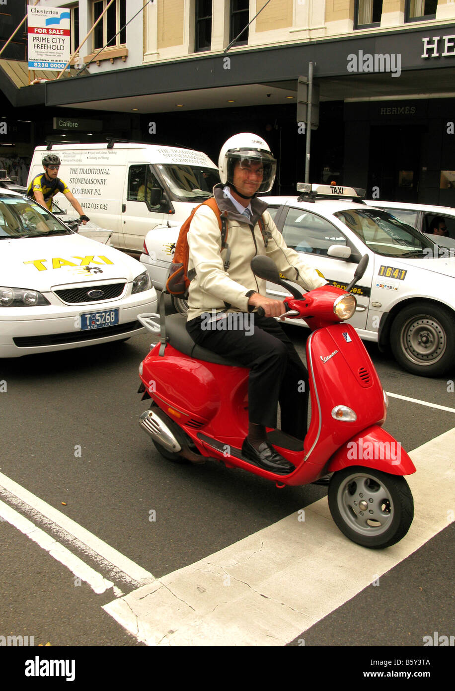 Un uomo che cavalca un rosso Vespa scooter nel traffico urbano Foto Stock