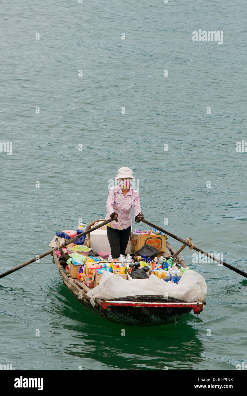Donna vendendo i suoi prodotti da una piccola barca a remi in Halong Bay, Vietnam Foto Stock