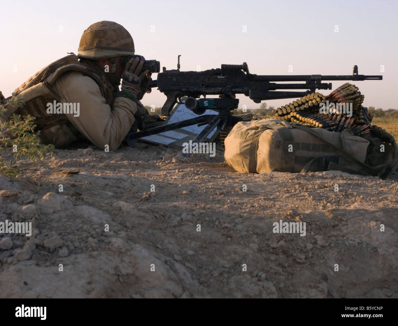 Provincia di Helmand Afghanistan soldato britannico che giace a terra guardando attraverso il binocolo con un obiettivo generale mitragliatrice Foto Stock
