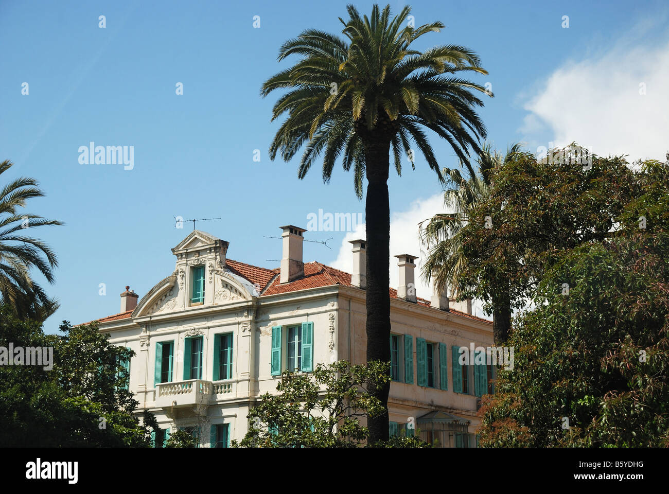 Residenza Mediterranea con persiane blu nel mezzo di alberi verdi e le alte palme blu cielo nuvoloso Francia Foto Stock