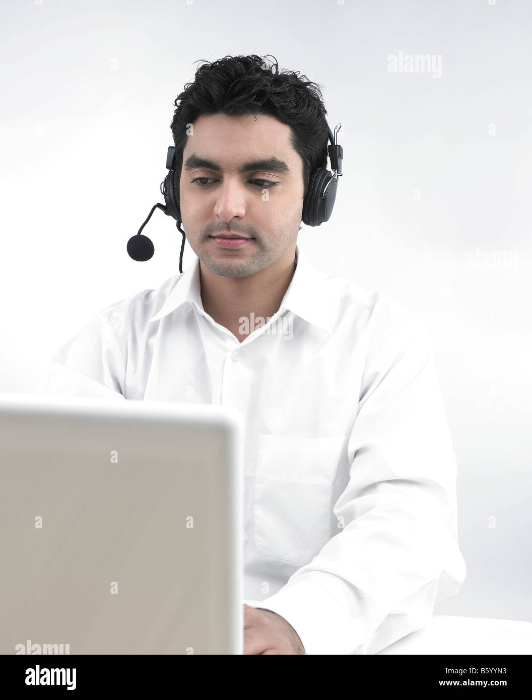 Uomo asiatico lavorando sul suo laptop che indossa le sue cuffie Foto Stock