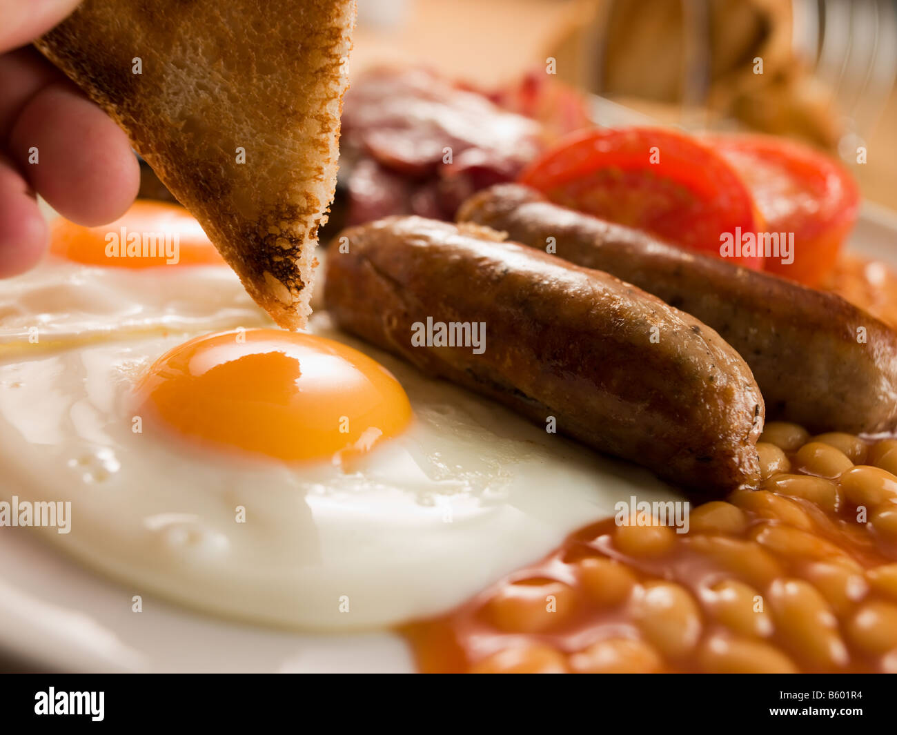 Toast di immersione in un uovo fritto su una colazione inglese completa Foto Stock
