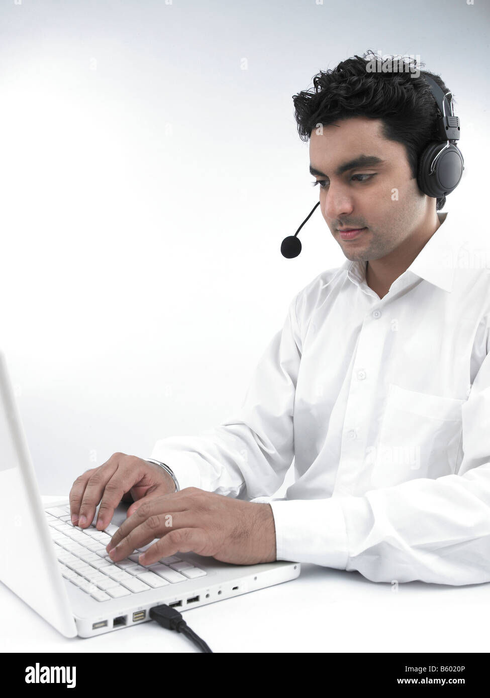 Uomo asiatico lavorando sul suo laptop che indossa le sue cuffie Foto Stock