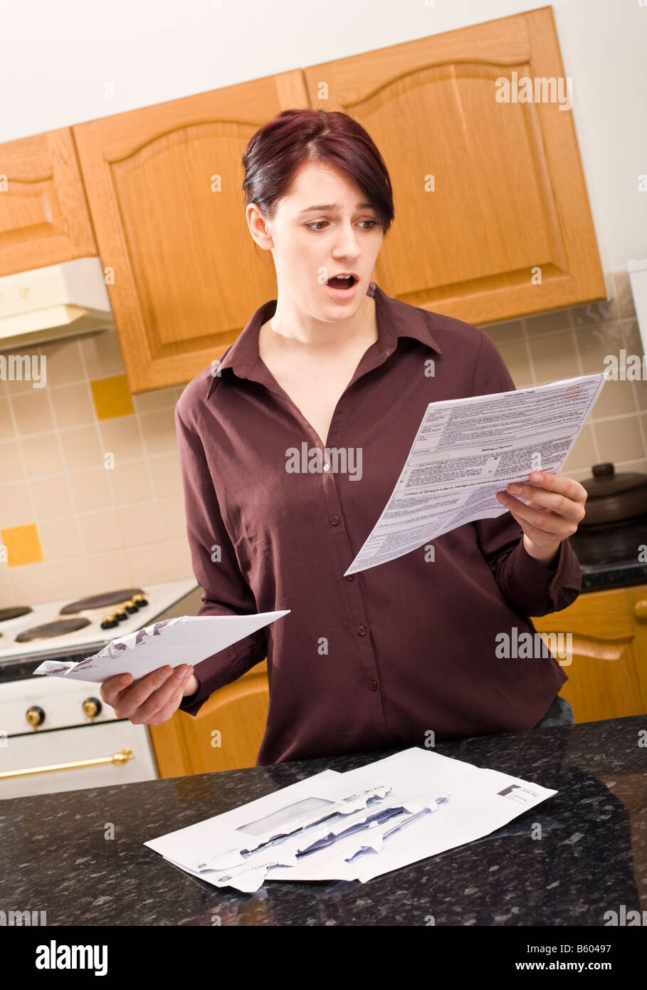 Giovane donna apre una lettera a casa e guarda in stato di shock con la dimensione del disegno di legge racchiusa MR PR Foto Stock