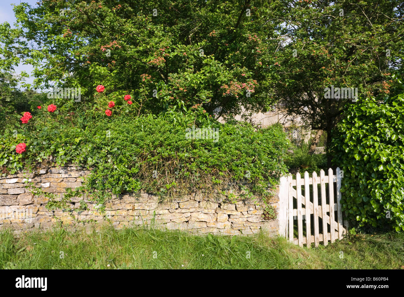 Il muro del giardino intorno un rustico cottage in pietra nel villaggio Costwold di Swinbrook, Oxfordshire Foto Stock
