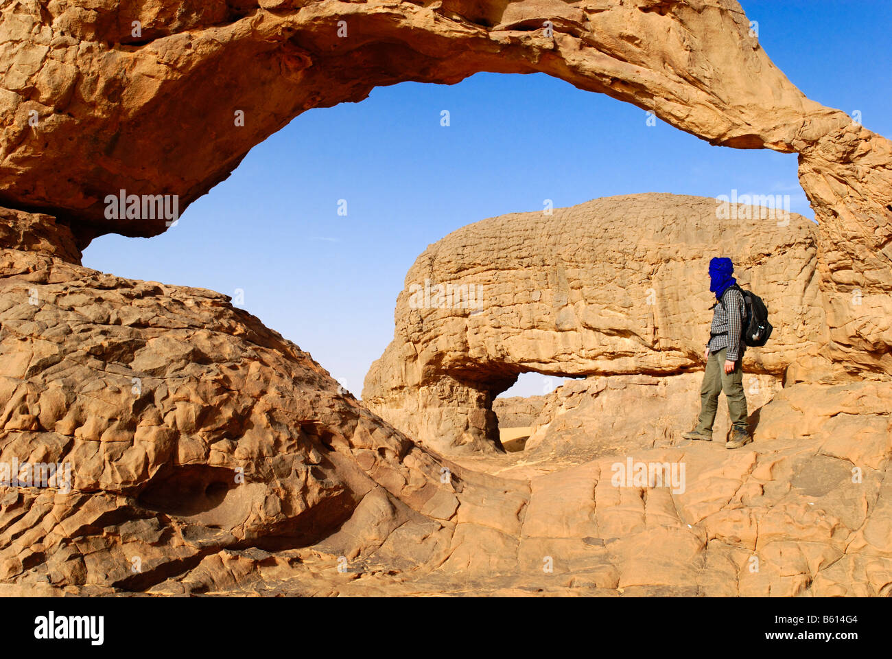 Uomo in piedi sotto la roccia arco di Youf Ahakit, Tassili du Hoggar, Wilaya Tamanrasset, Algeria, deserto del Sahara Foto Stock