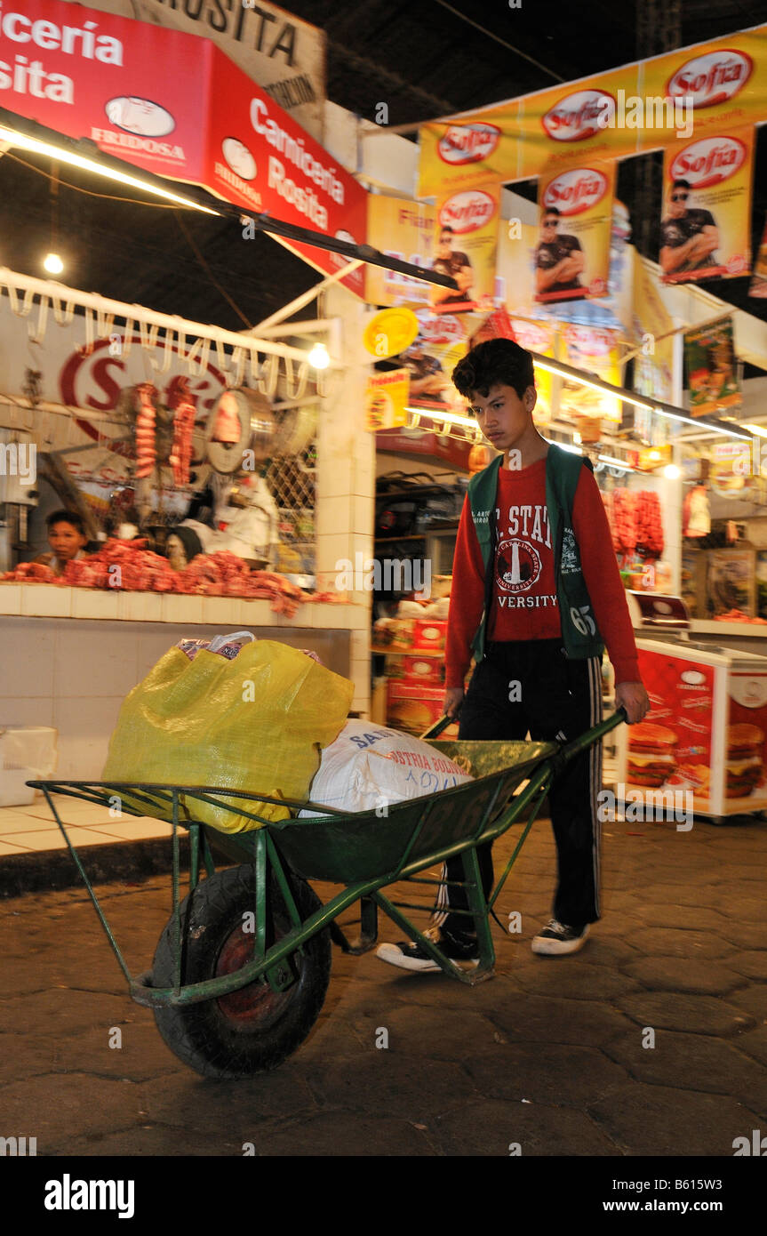Il lavoro minorile, ragazzo di trasportare i clienti " gli acquisti utilizzando una ruota barrow al mercato locale, Santa Cruz, Bolivia, Sud America Foto Stock