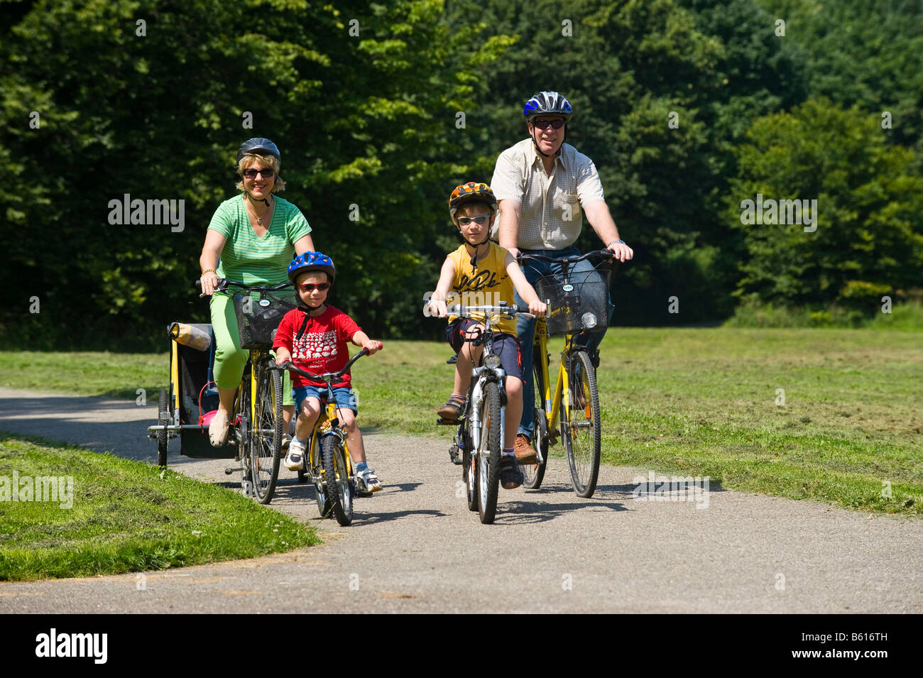 Famiglia con 2 bambini di andare in bicicletta attraverso il parco, indossare i caschi Foto Stock