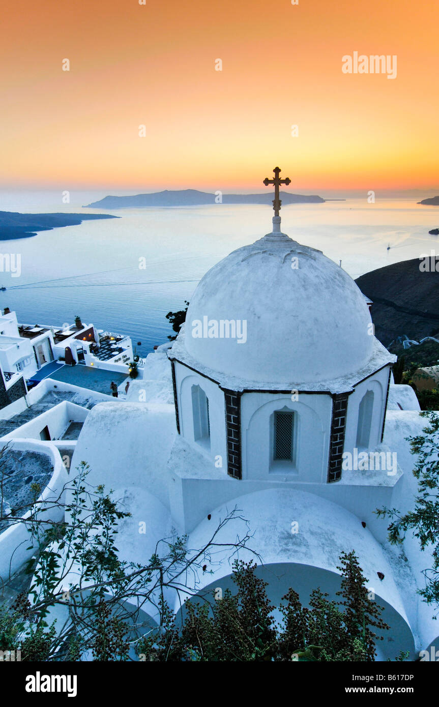 Bianco chiesa a cupola con una croce al tramonto davanti al mare e l'isola vulcanica di Nea Kameni, Santorini, Cicladi Grecia Foto Stock