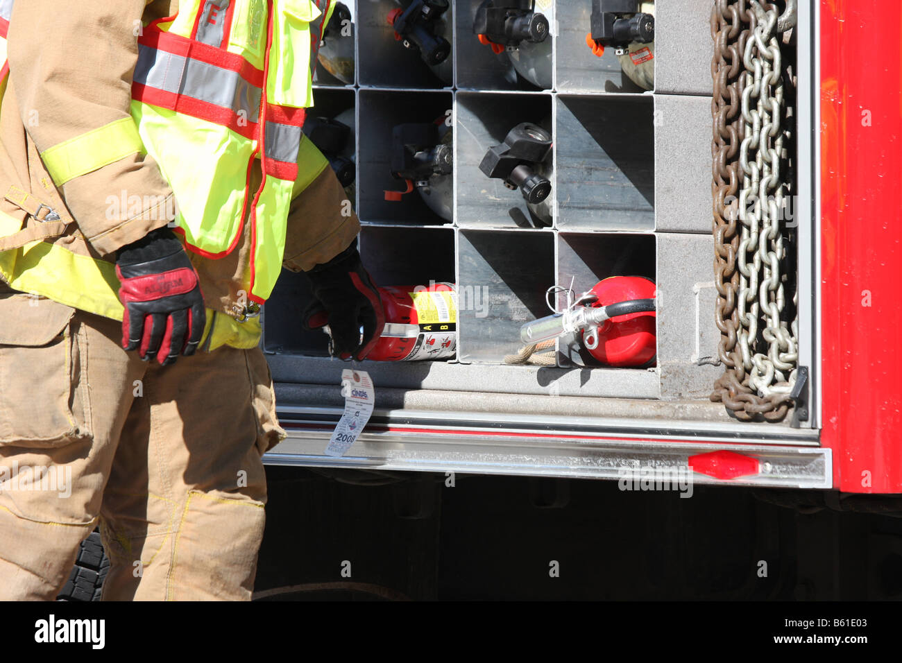 Un vigile del fuoco afferrando un estintore al di fuori del vano del firetruck Foto Stock