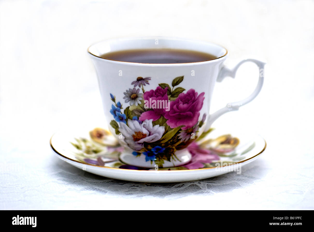 Una tazza di caffè in una tazza con motivi floreali e piattino, poggiante su una tovaglia di pizzo. Foto Stock