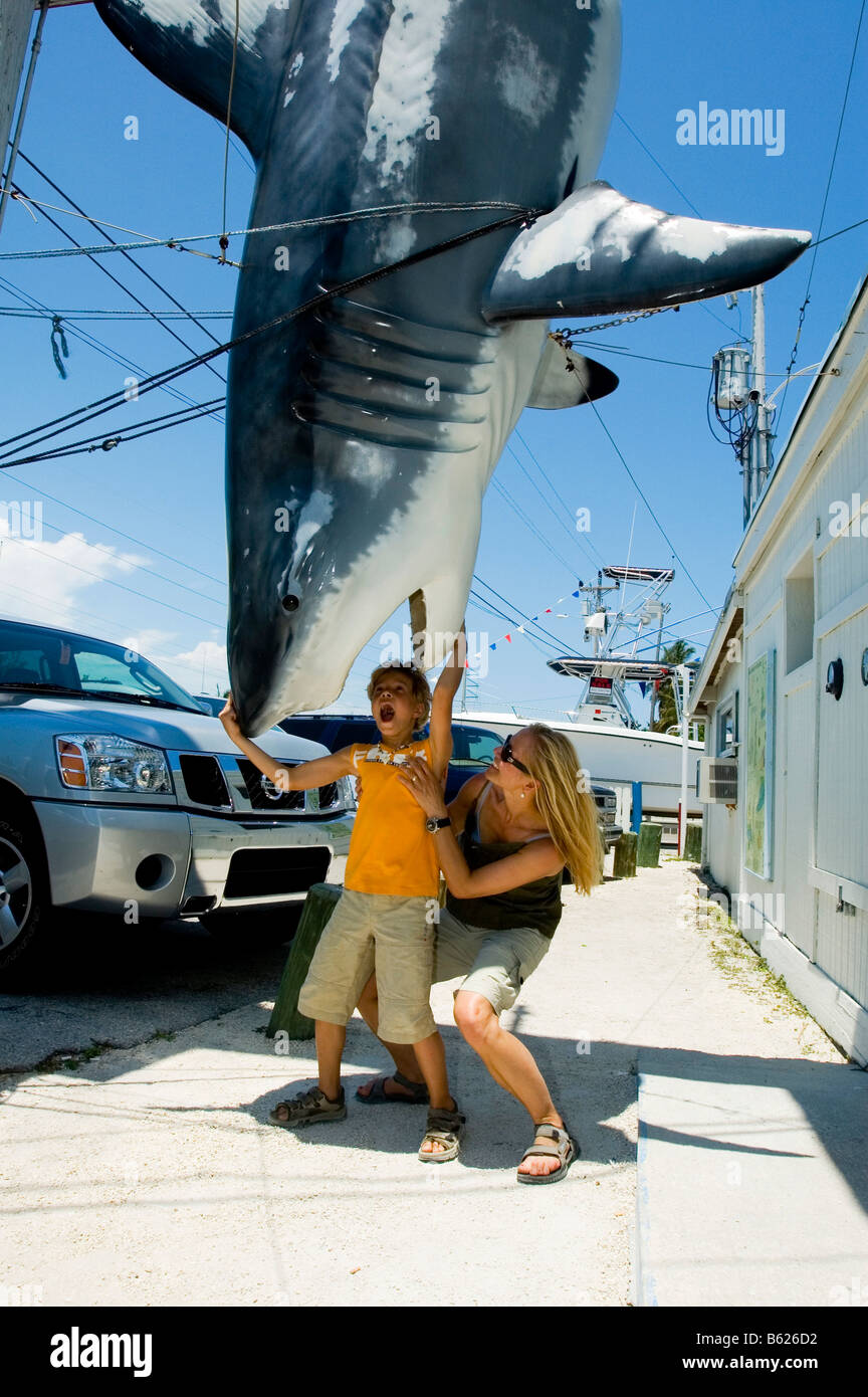 Donna e bambino in piedi sotto un mock-up di un grande squalo bianco, Islamorada, Florida Keys, Florida, Stati Uniti d'America Foto Stock