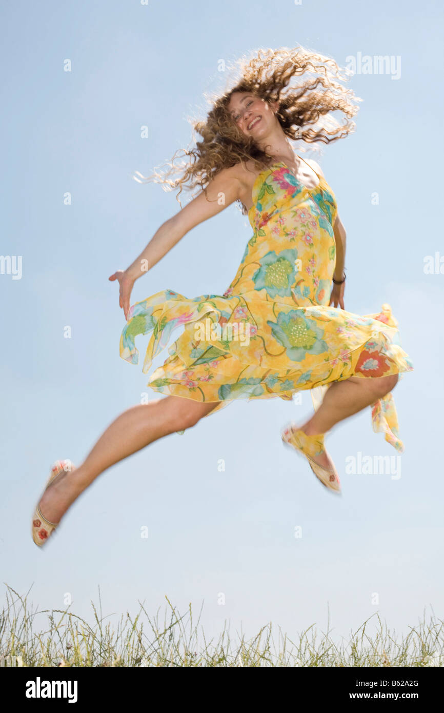 Giovane donna con capelli lunghi che indossa un abito giallo jumping davanti a un cielo blu Foto Stock