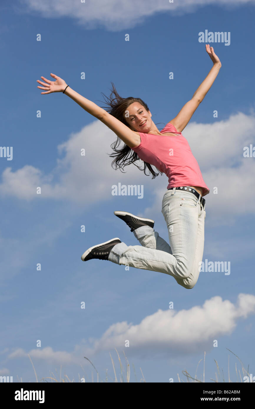 Giovani dai capelli scuri salto donna nella parte anteriore del cielo blu Foto Stock