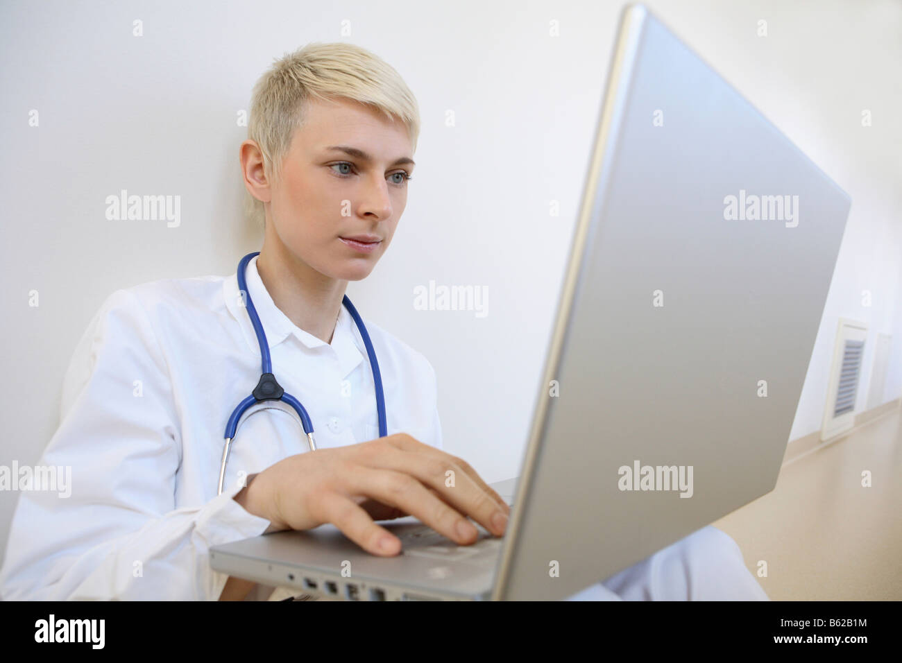 Giovane medico con uno stetoscopio inserendo la sua relazione in un notebook Foto Stock