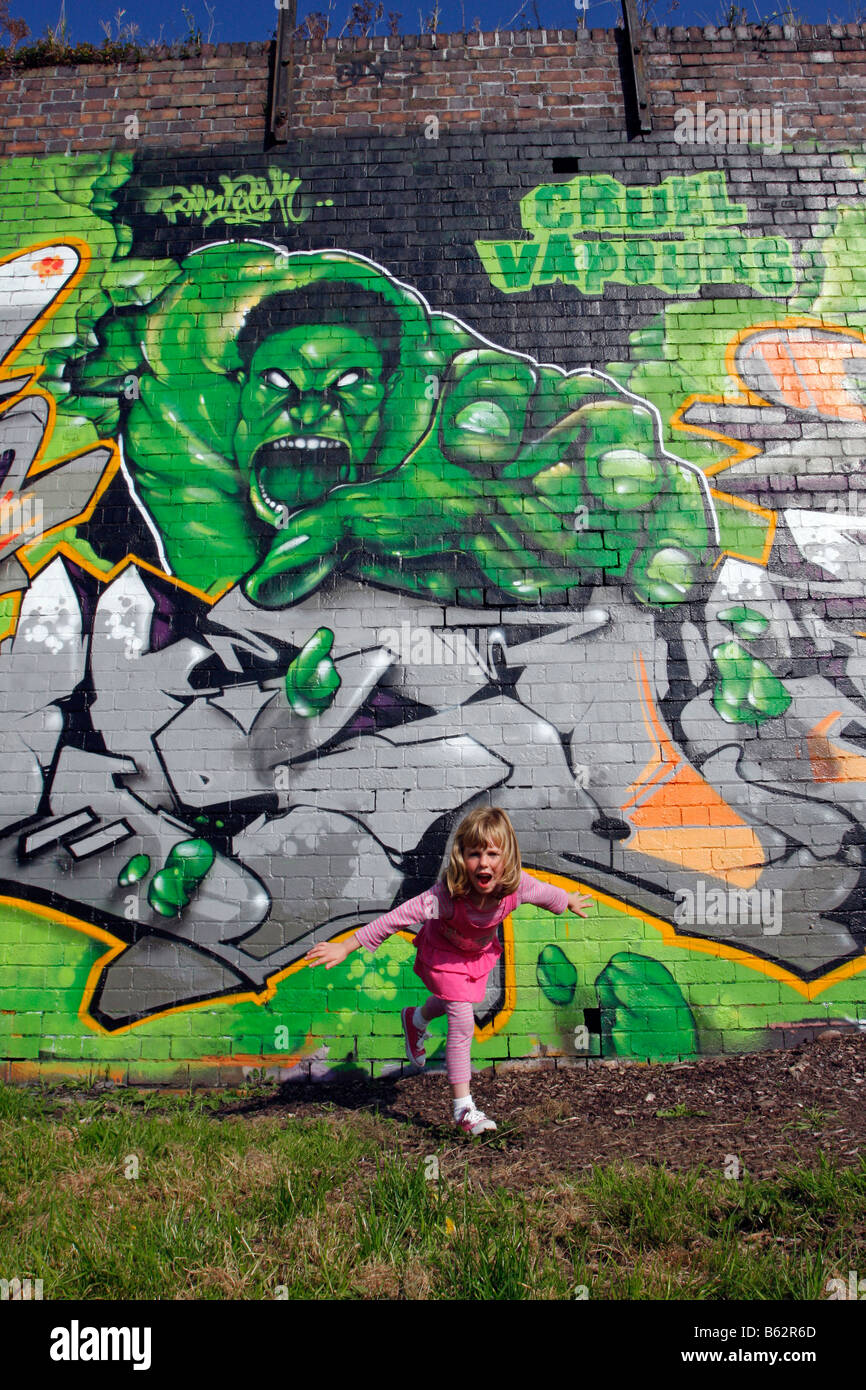 Ragazza che figurano a fuggire da una foto di graffiti spruzzato su una parete Incredible Hulk escape Foto Stock