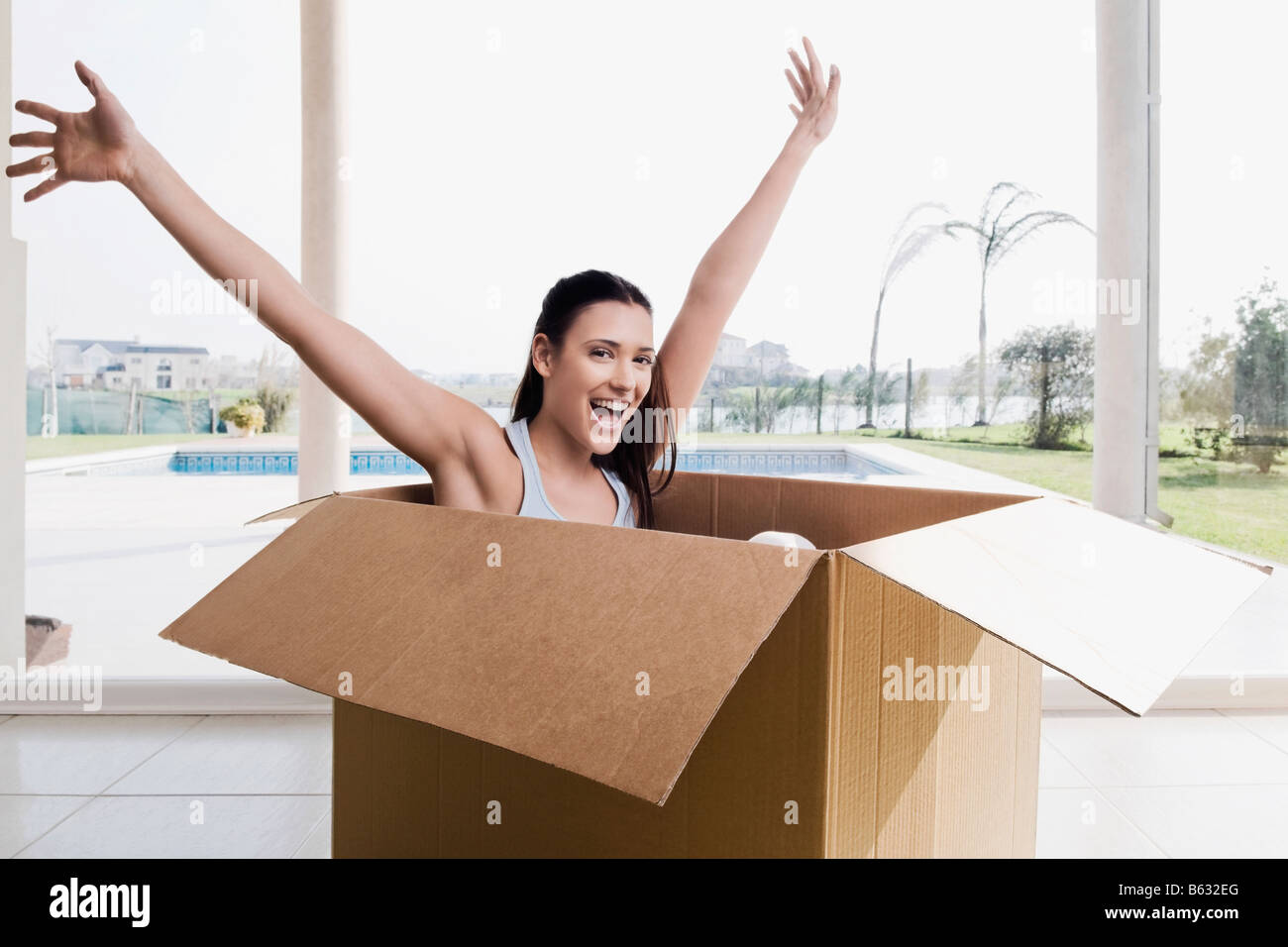 Ritratto di una giovane donna seduta in una scatola di cartone con le braccia sollevate Foto Stock