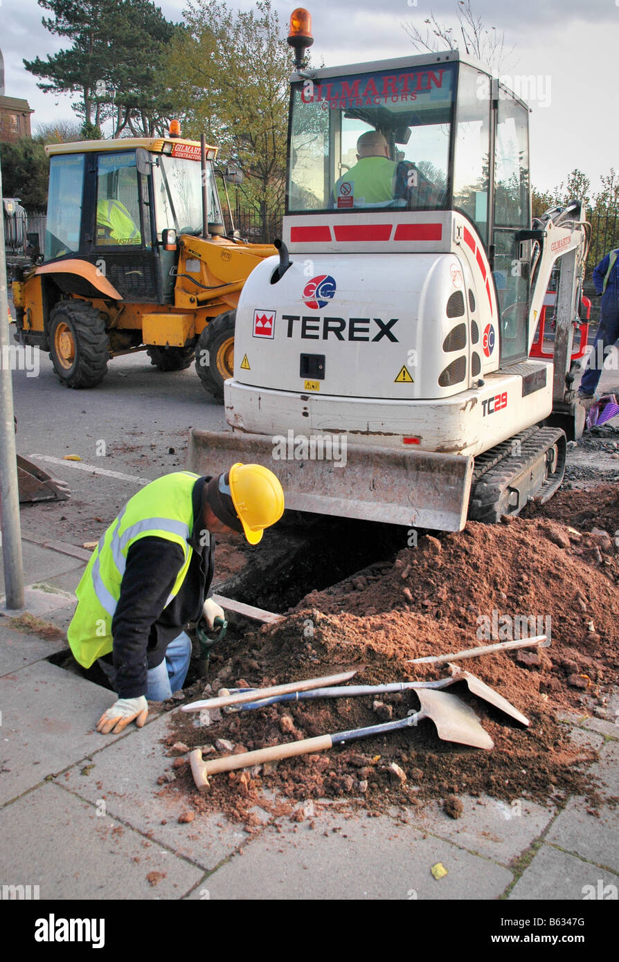 Operai scavi sul marciapiede e la strada per stabilire nuovi tubi. Foto Stock