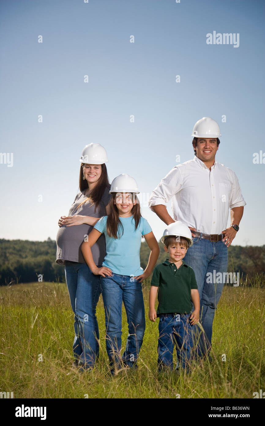 Famiglia di quattro piedi insieme in un campo presso il sito del loro futuro home site, indossare copricapi rigidi. Foto Stock