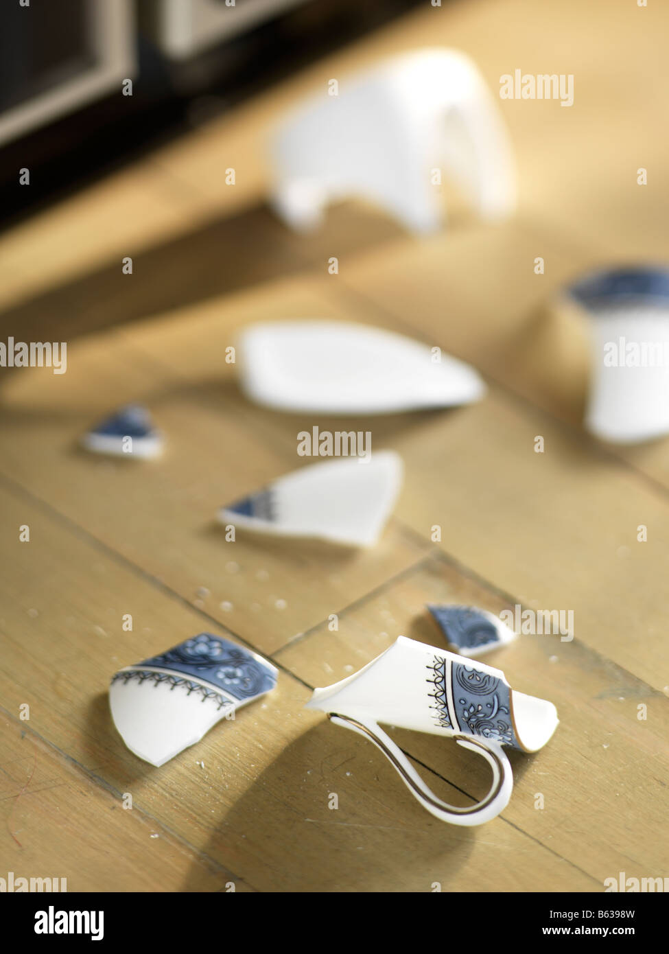 Osso rotto cina tazza da caffè su un pavimento di legno duro con l'angolo di un acciaio inossidabile frigo in t egli lo sfondo Foto Stock