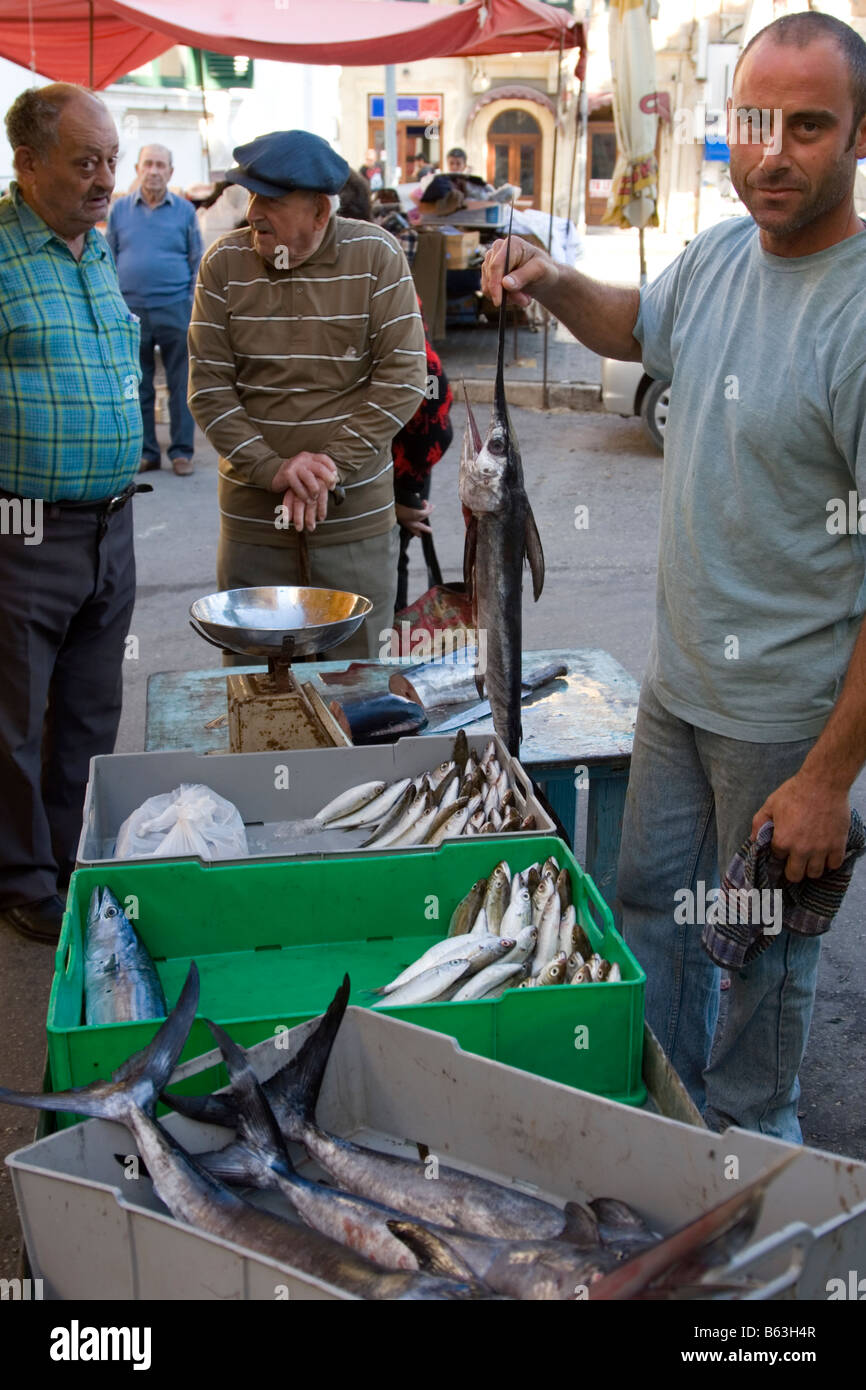 Un pescivendolo con un giovane pesce spada a una pressione di stallo di pesce al mercato all'aperto in Rabat Gozo Malta Foto Stock