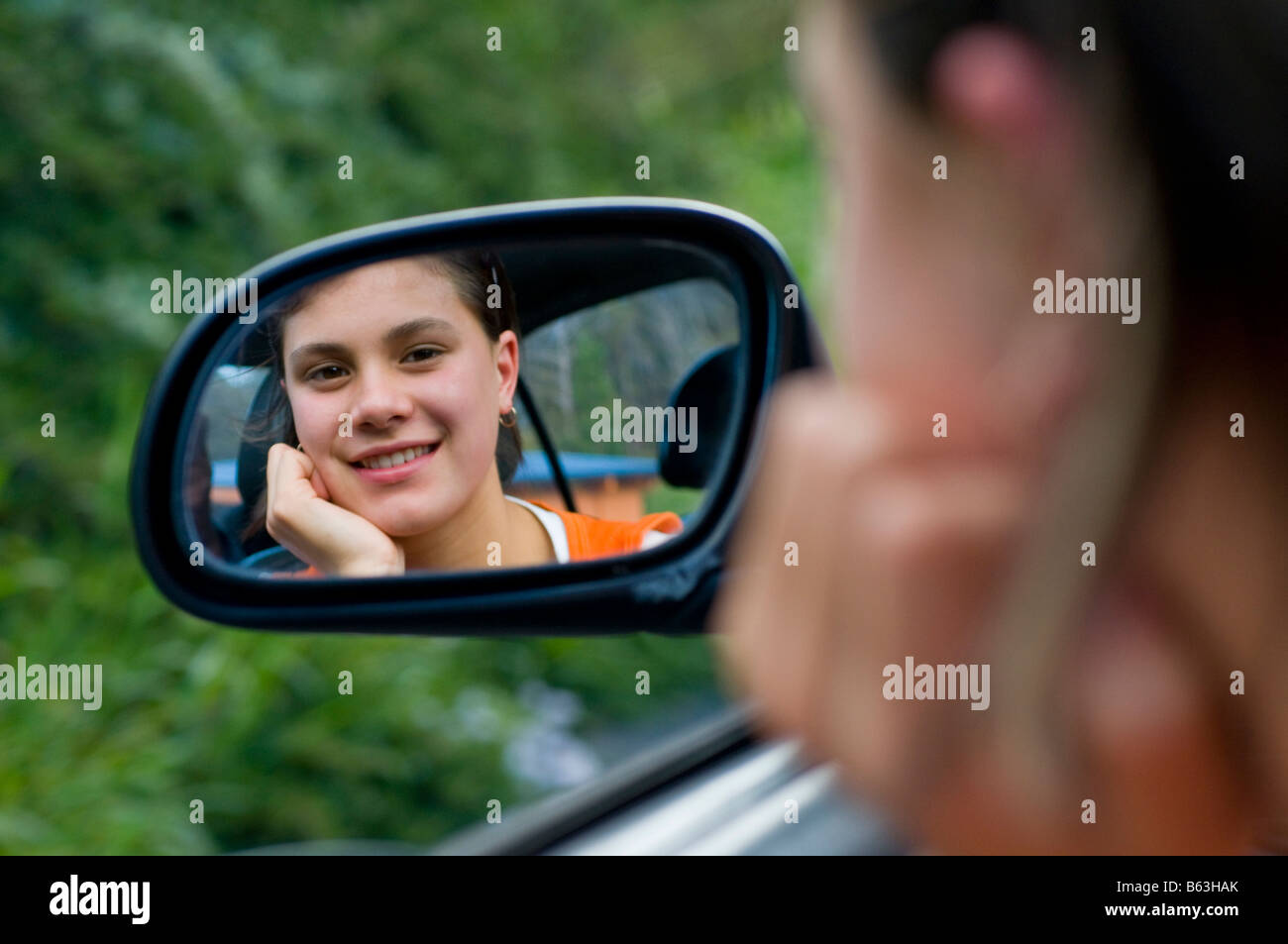 Sorridente giovane ragazza adolescente cercando nello specchietto retrovisore della macchina Foto Stock