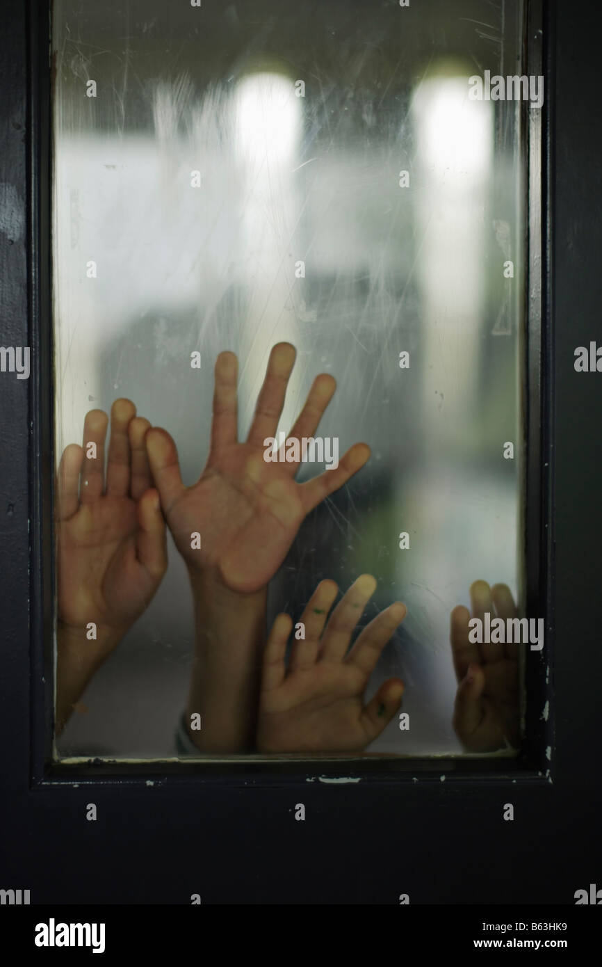 Le mani della bambina di cinque anni e sei anni di old boy contro il pannello di vetro della porta Foto Stock