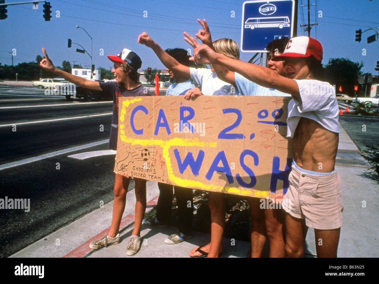 Teen boys tenere premuto segno promozione car wash per raccogliere fondi per la loro squadra di calcio dei materiali di consumo. Foto Stock