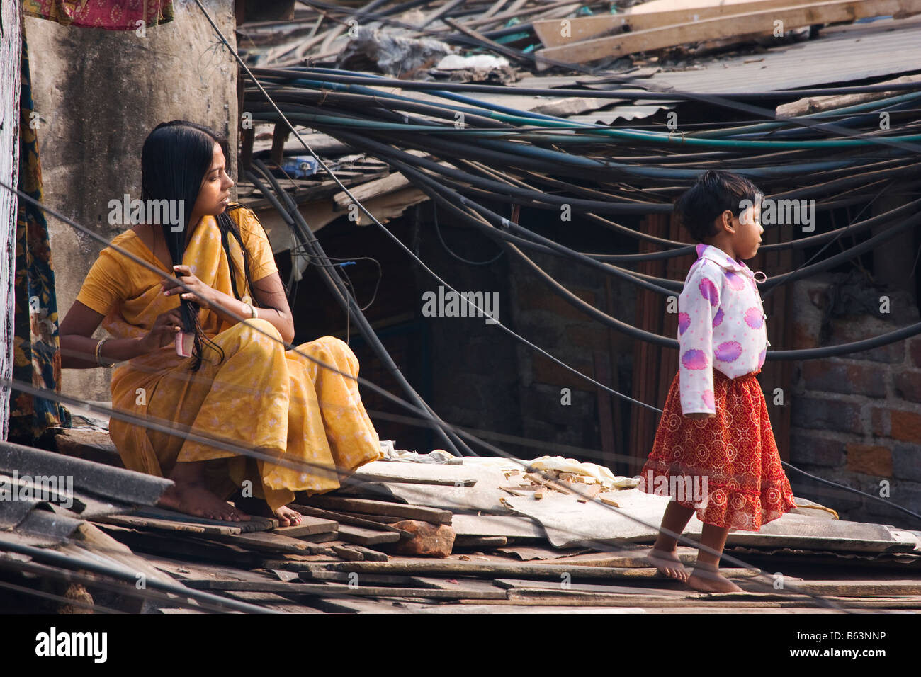Una donna di pettini i capelli mentre si siede tra i molti cavi di alimentazione alimentazione di una baraccopoli di Kolkata India Foto Stock