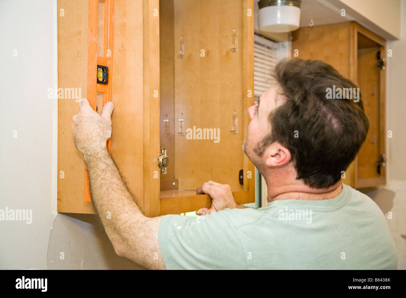 Carpenter installazione di acero solido mobili da cucina utilizzando un livello per verificare il suo lavoro Foto Stock