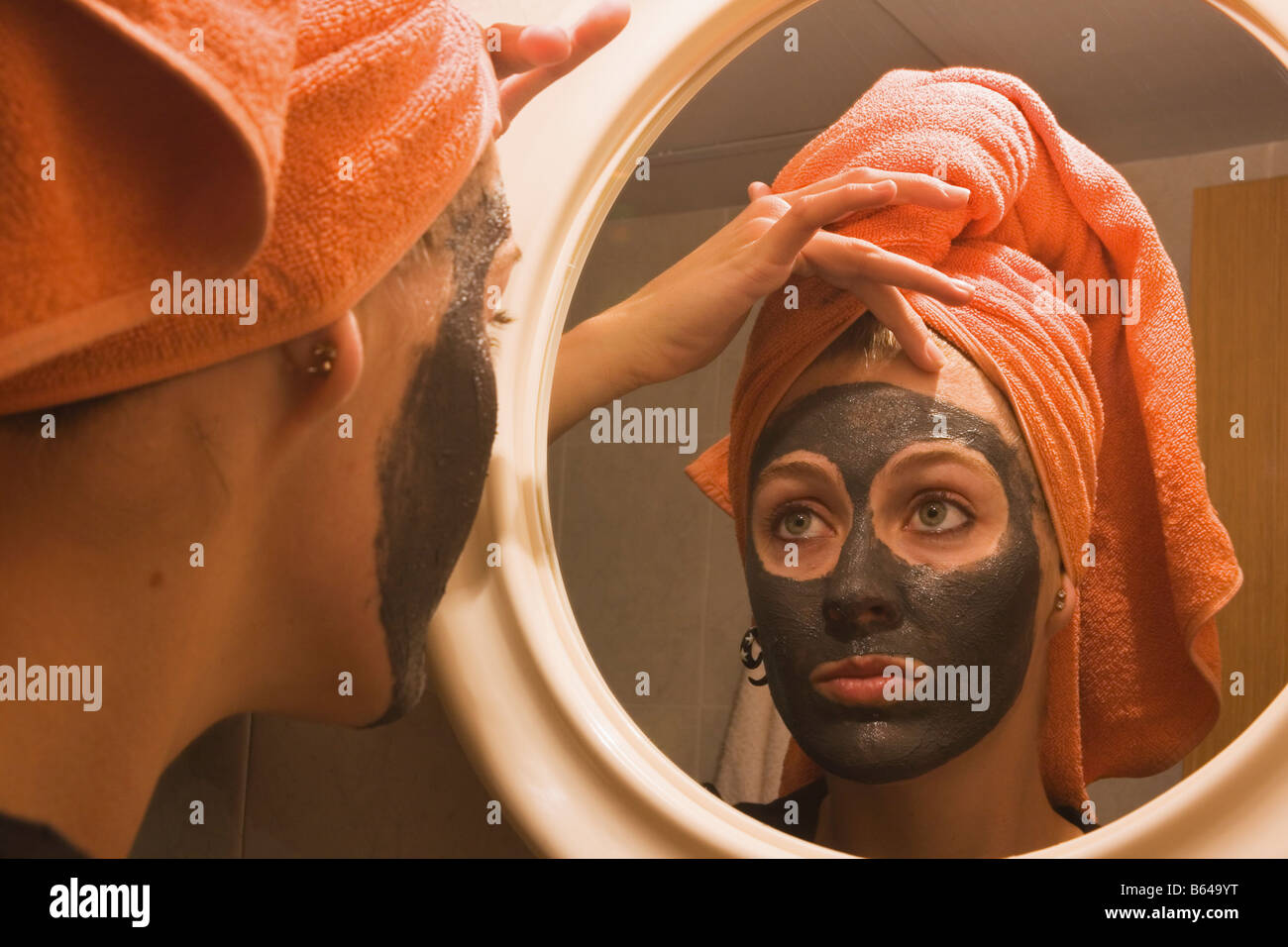 Giovane donna con la spugnetta esfoliante per il viso maschera guardando a se stessa e a specchio Foto Stock