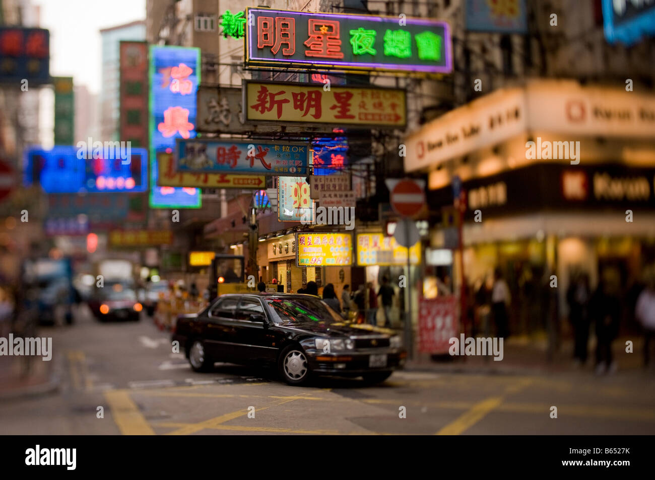 Un auto nera scorre lungo un distretto di Kowloon street illuminati da luci al neon di Hong Kong Foto Stock
