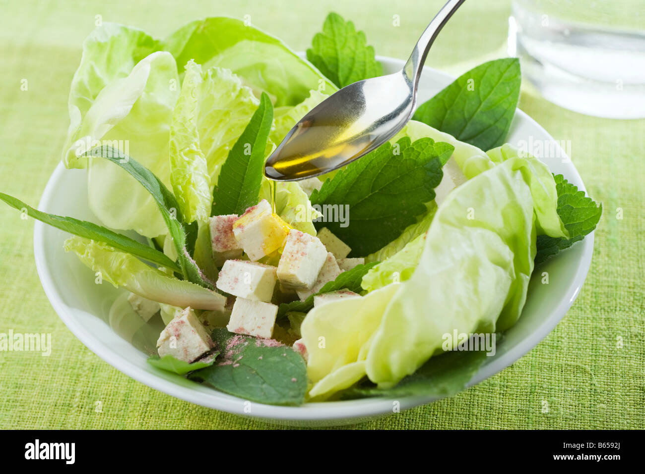 Cucchiaio drizzling olio d'oliva su insalata di verdure miste e i cubetti di tofu Foto Stock