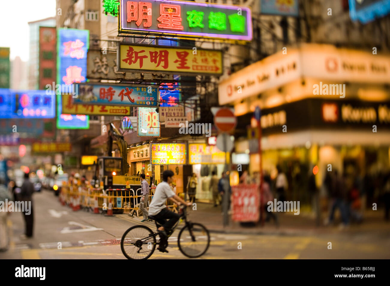 Un uomo che cavalca il suo ciclo lungo un distretto di Kowloon street illuminati da luci al neon di Hong Kong Foto Stock