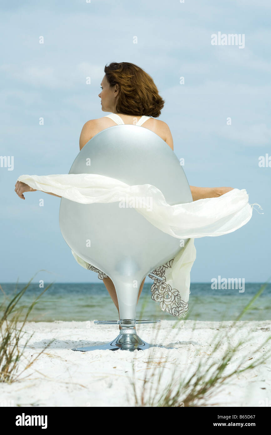 Donna seduta nella sedia sulla spiaggia, guardando a vista, sciarpa soffia nella brezza Foto Stock