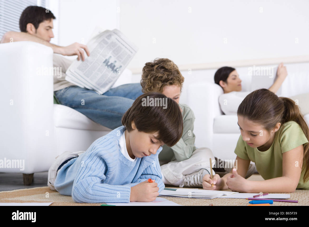 I bambini Colorare sul pavimento nel soggiorno, i genitori la lettura in background Foto Stock