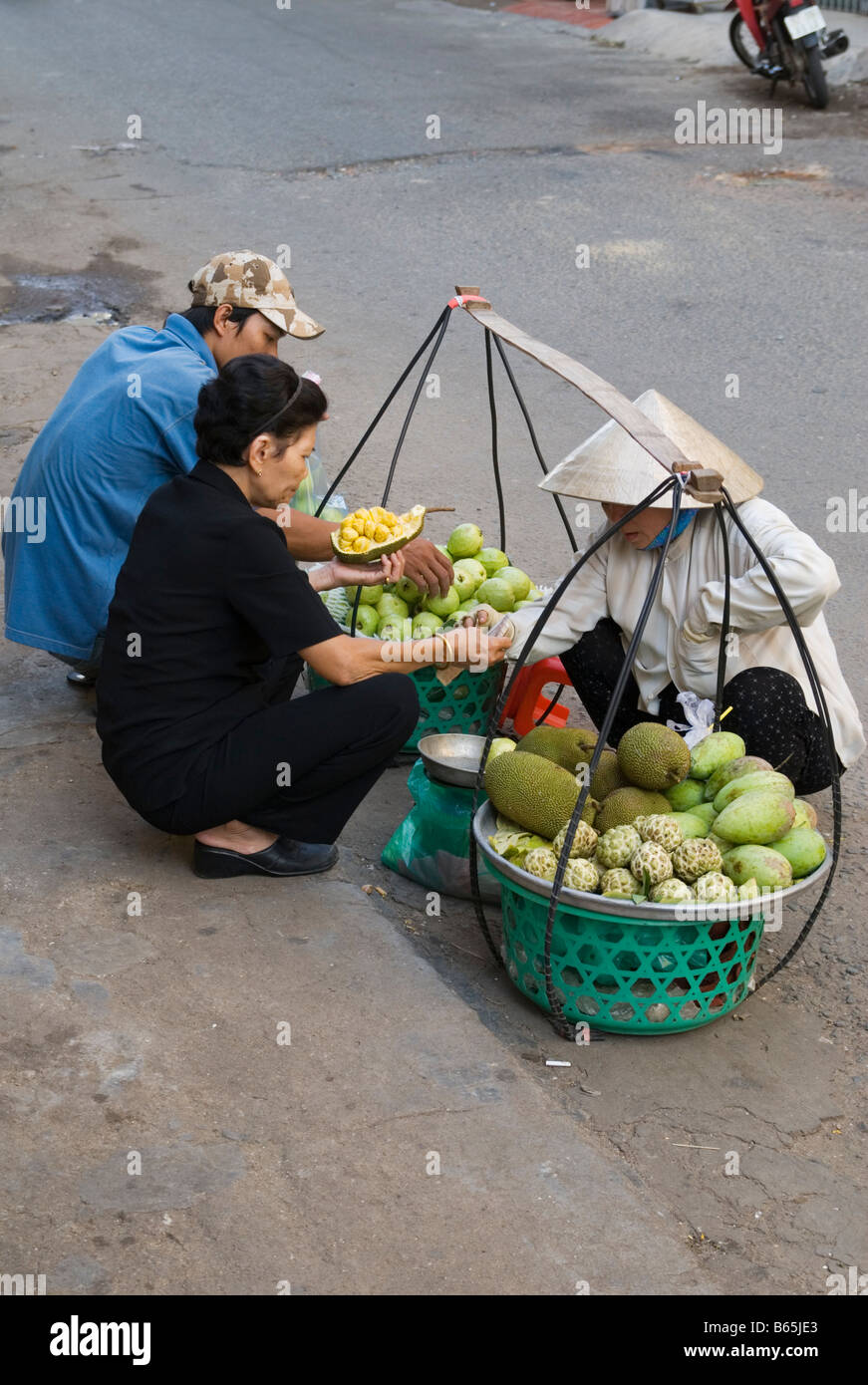 Squatting street trader indossando una foglia conica hat, Ho Chi Minh City, Vietnam Foto Stock