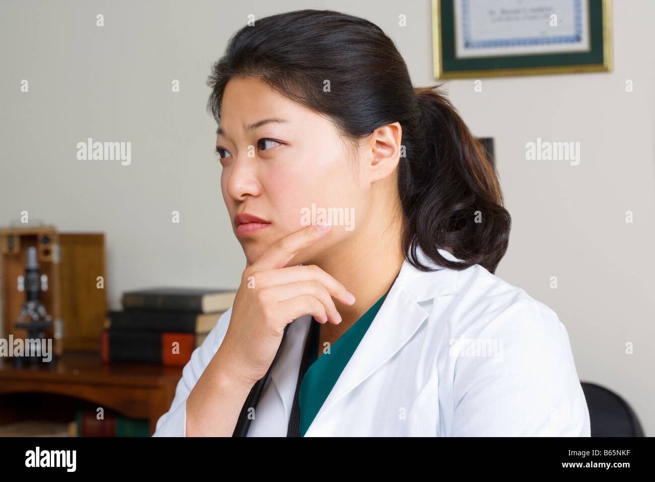 Donna asiatica del pensiero medico nel suo ufficio. Foto Stock