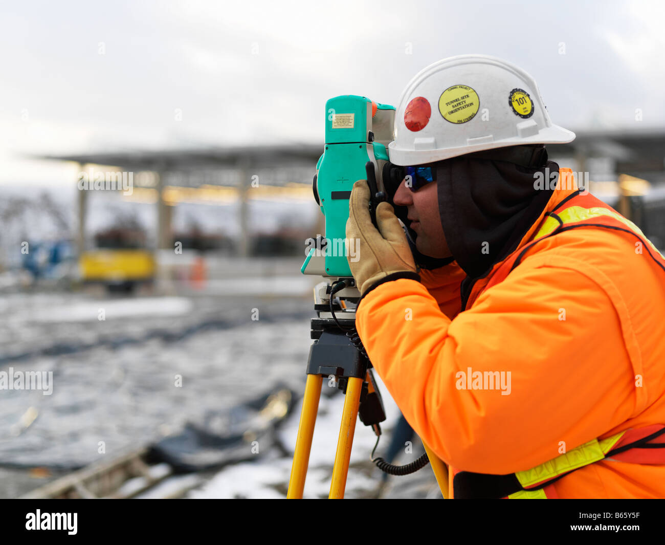 Costruzione sito in inverno con un geometra tenendo una lettura su una digitale teodolite di transito Foto Stock