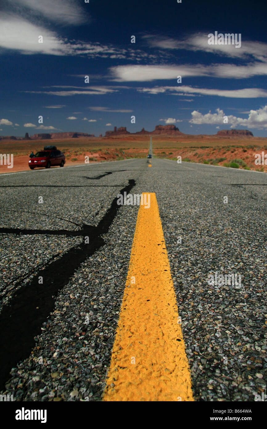 Closeup 'roadkill-eye-view' della superficie stradale guardando giù giallo linea di mezzeria della lunga strada diritta verso mesas Foto Stock
